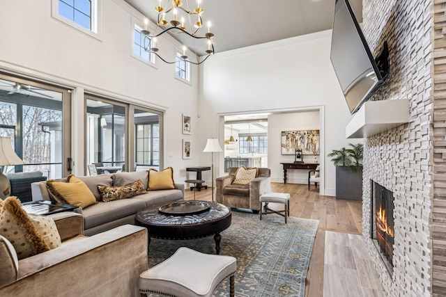 living area with baseboards, light wood-style flooring, an inviting chandelier, a high ceiling, and a fireplace