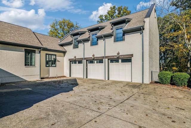 exterior space featuring a garage, a shingled roof, concrete driveway, and brick siding