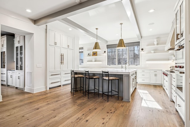 kitchen with glass insert cabinets, a center island with sink, white cabinetry, and light countertops