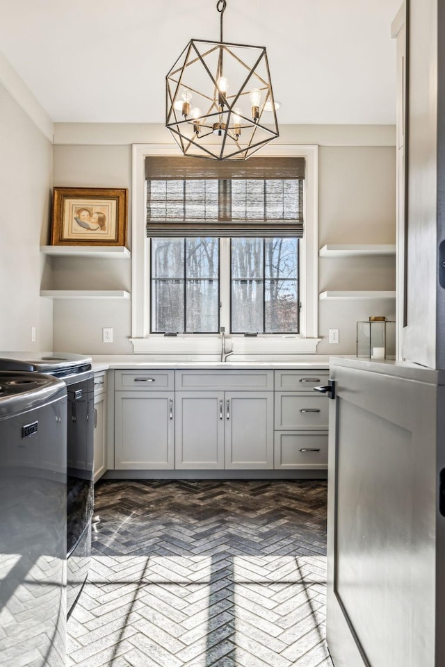 kitchen featuring pendant lighting, gray cabinets, light countertops, stove, and an inviting chandelier