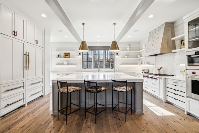 kitchen with a breakfast bar, open shelves, light countertops, glass insert cabinets, and an island with sink