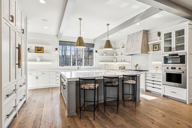 kitchen with an island with sink, glass insert cabinets, light countertops, white cabinetry, and open shelves