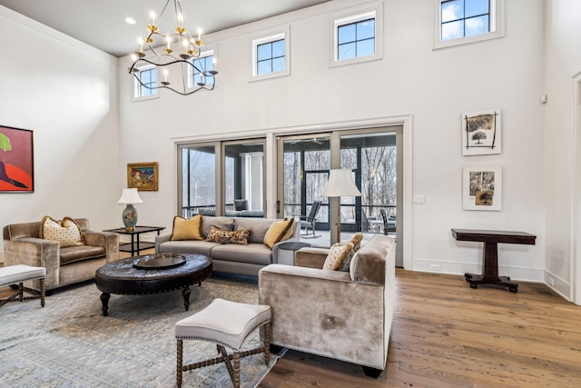 living area with a high ceiling, an inviting chandelier, wood finished floors, and baseboards