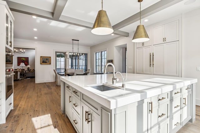 kitchen with an island with sink, white cabinets, hanging light fixtures, and light countertops