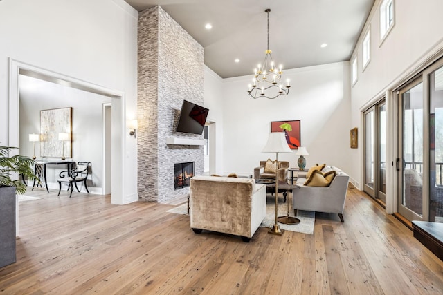 living area with light wood-type flooring, a high ceiling, a chandelier, and a stone fireplace