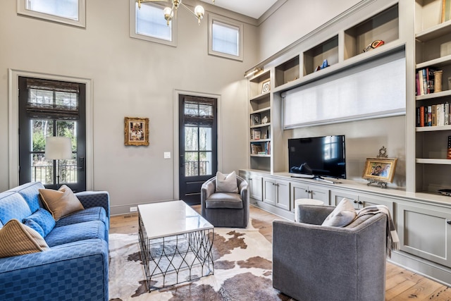 living room featuring a towering ceiling, light wood-style floors, built in shelves, and baseboards