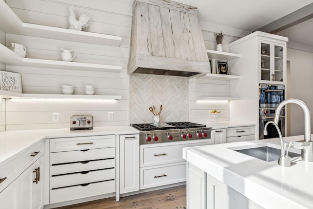 kitchen featuring custom range hood, stainless steel appliances, light countertops, white cabinetry, and open shelves