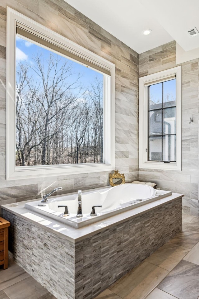 bathroom featuring a healthy amount of sunlight, visible vents, and tile walls