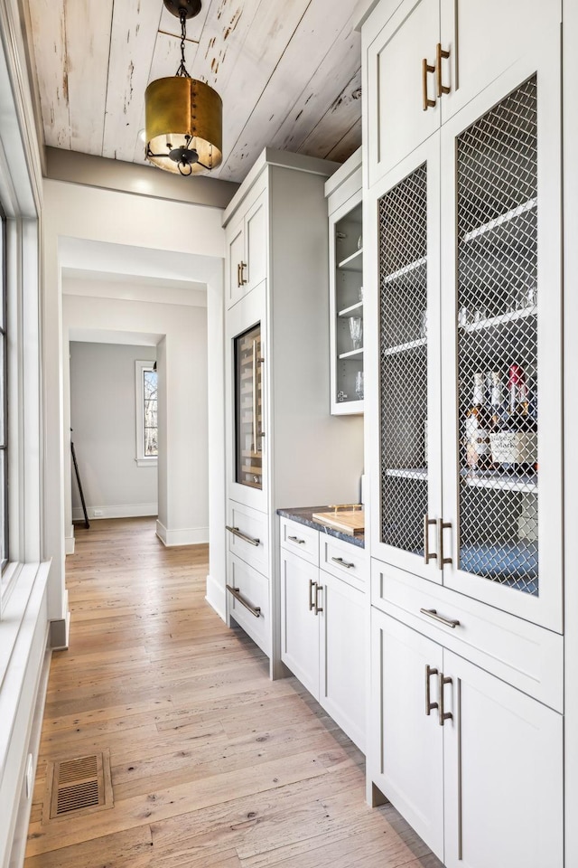 bar with hanging light fixtures, light wood-style flooring, visible vents, and baseboards