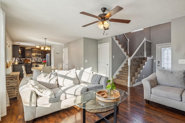 living room featuring dark wood-style floors, stairs, baseboards, and ceiling fan with notable chandelier