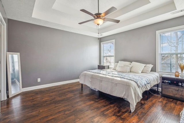 bedroom with hardwood / wood-style flooring, a raised ceiling, visible vents, and baseboards