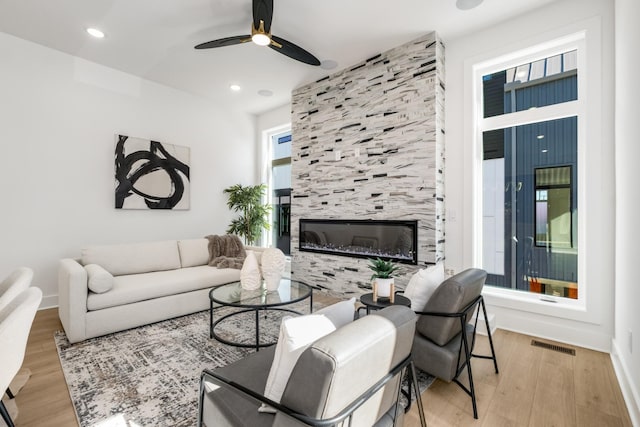 living room with baseboards, visible vents, a ceiling fan, a tile fireplace, and light wood-type flooring