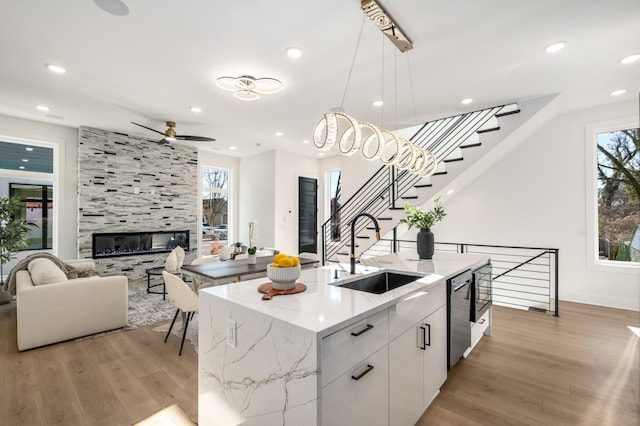 kitchen with a sink, white cabinetry, open floor plan, hanging light fixtures, and an island with sink