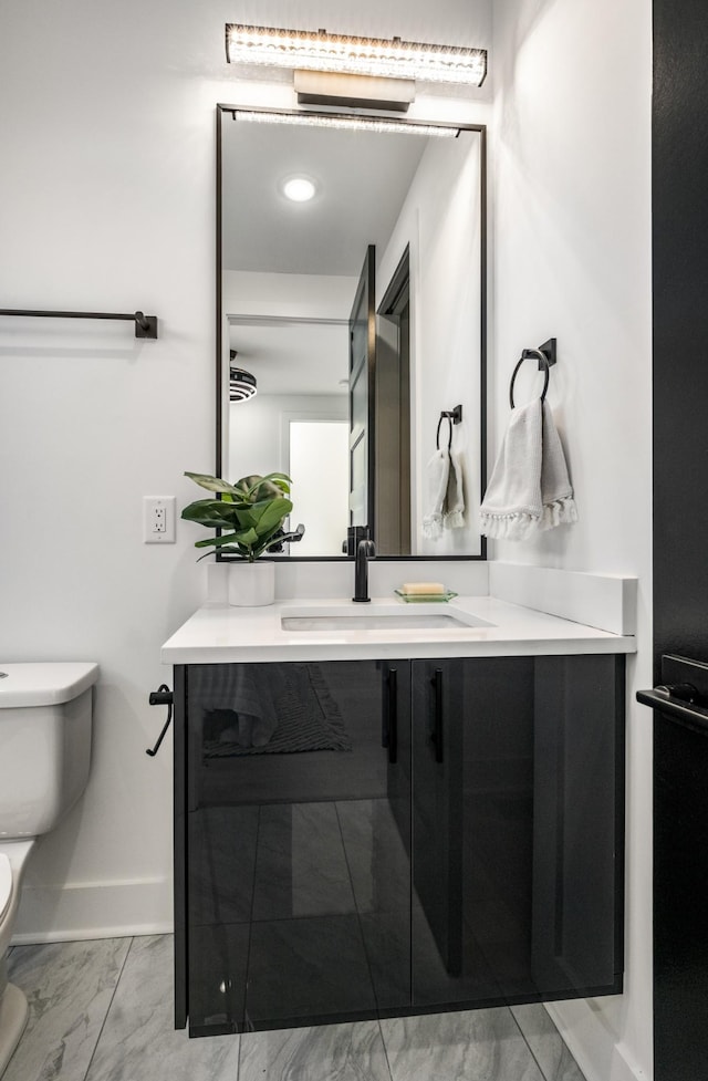 bathroom featuring toilet, marble finish floor, baseboards, and vanity