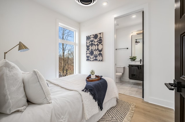 bedroom featuring light wood-style floors, baseboards, visible vents, and connected bathroom
