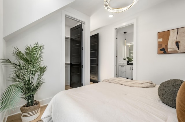bedroom featuring baseboards, ensuite bath, and wood finished floors