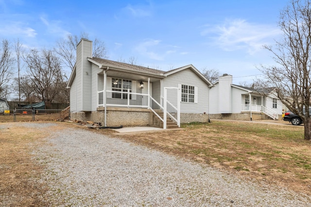 view of front of property with gravel driveway, a chimney, covered porch, a front yard, and fence