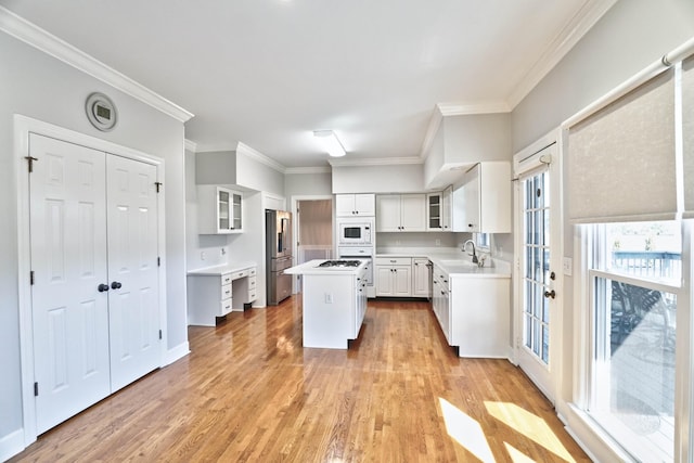 kitchen with light wood-style flooring, white microwave, a kitchen island, a sink, and stainless steel fridge