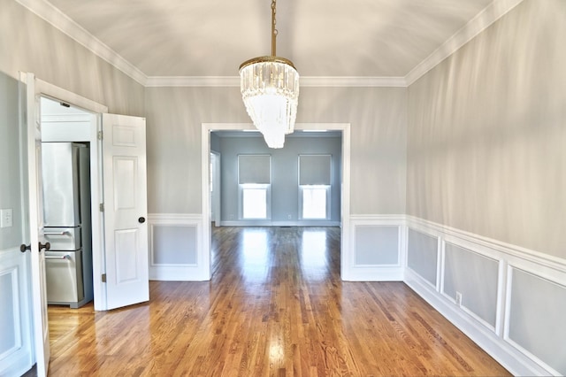 unfurnished dining area featuring a chandelier, ornamental molding, wood finished floors, and a decorative wall