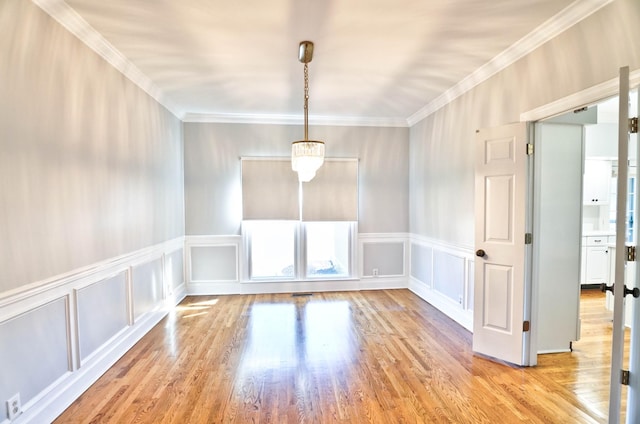 unfurnished dining area featuring light wood-type flooring, ornamental molding, and a decorative wall