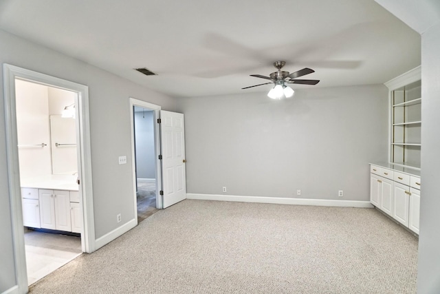 interior space with light carpet, baseboards, visible vents, ensuite bath, and ceiling fan