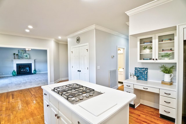 kitchen with a fireplace, light countertops, stainless steel gas stovetop, glass insert cabinets, and built in study area