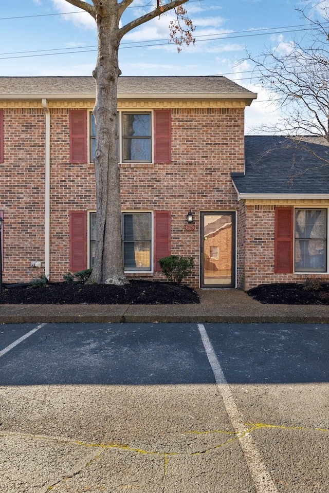 view of front facade featuring roof with shingles, uncovered parking, and brick siding