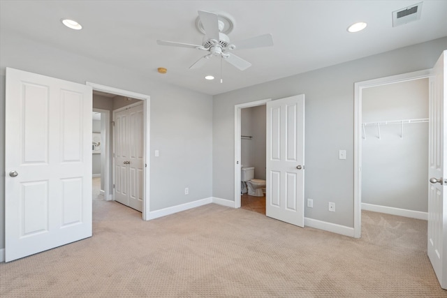 unfurnished bedroom featuring a walk in closet, light colored carpet, visible vents, and baseboards