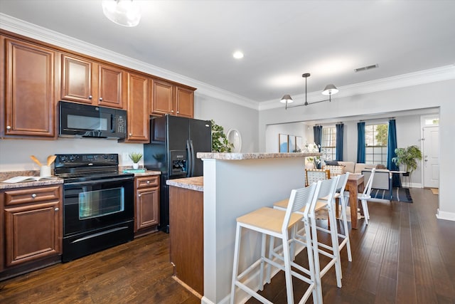 kitchen featuring visible vents, a kitchen breakfast bar, black appliances, brown cabinetry, and crown molding