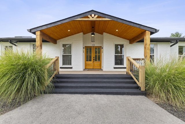 view of exterior entry with covered porch, french doors, and brick siding