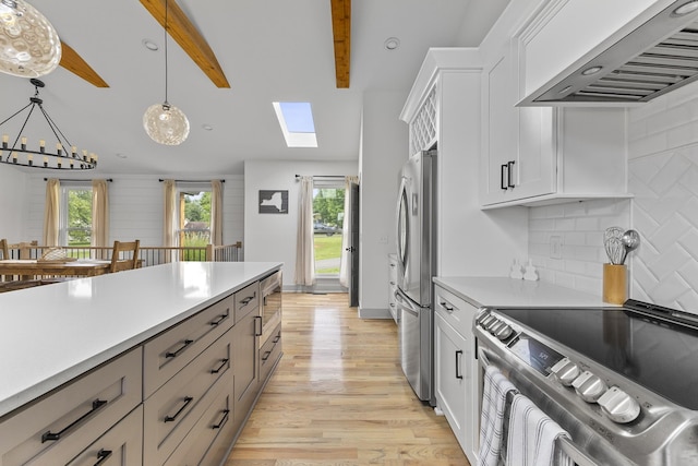 kitchen with appliances with stainless steel finishes, light countertops, hanging light fixtures, and wall chimney range hood