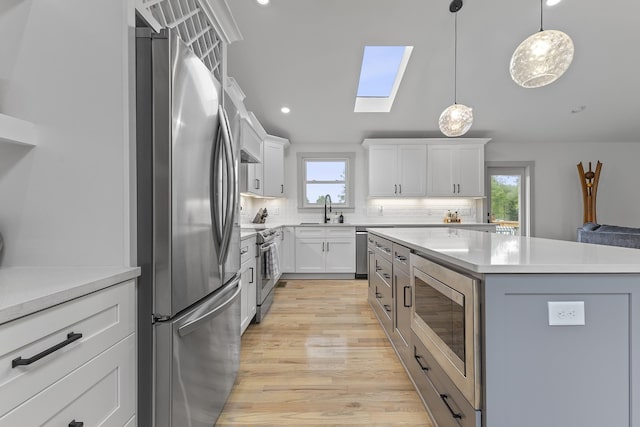 kitchen with a kitchen island, appliances with stainless steel finishes, light countertops, white cabinetry, and a sink