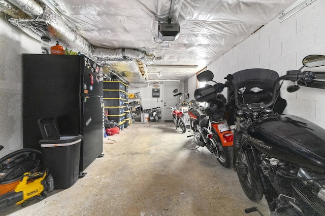 garage with a garage door opener, freestanding refrigerator, and concrete block wall