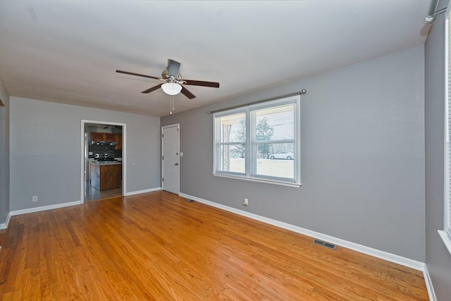 spare room with ceiling fan, light wood finished floors, visible vents, and baseboards