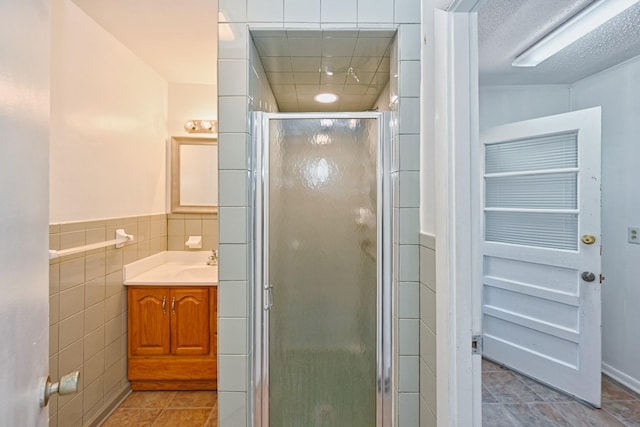 full bathroom featuring tile patterned floors, a textured ceiling, vanity, a shower stall, and tile walls