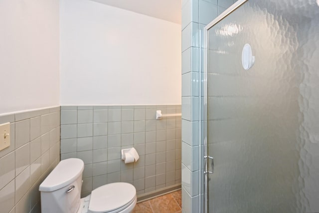 full bath featuring toilet, a wainscoted wall, tile patterned flooring, a shower stall, and tile walls