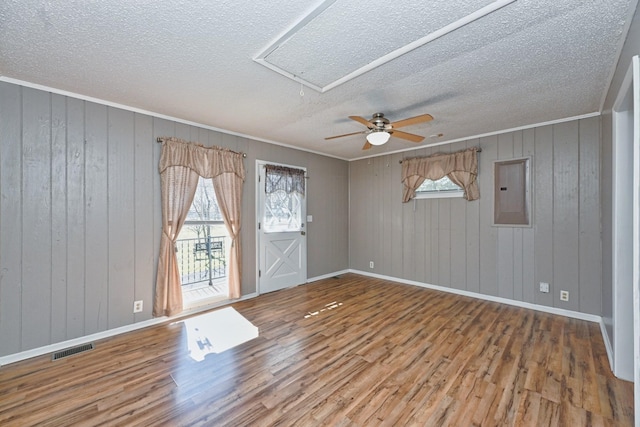 unfurnished room with a wealth of natural light, electric panel, visible vents, and wood finished floors