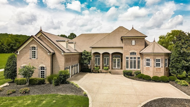 french provincial home with a garage, concrete driveway, and brick siding