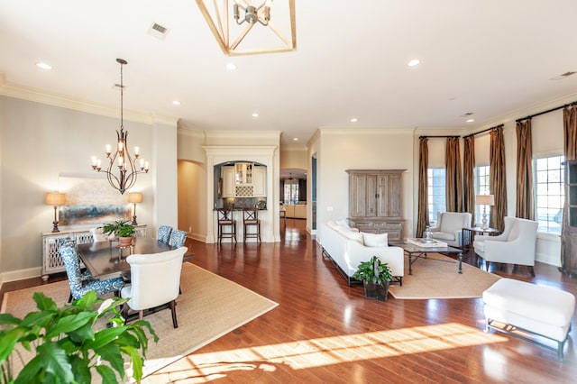 living area with crown molding, arched walkways, a notable chandelier, and wood finished floors