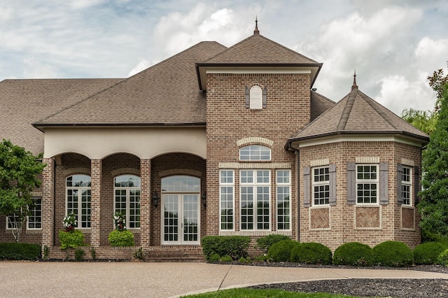 french country style house with french doors, brick siding, and roof with shingles