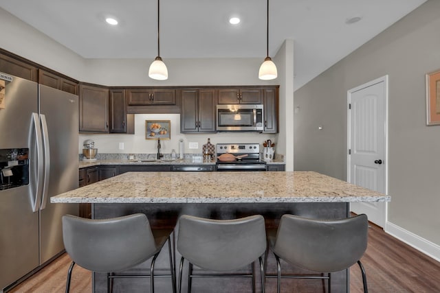 kitchen with dark brown cabinetry, appliances with stainless steel finishes, wood finished floors, a kitchen bar, and a sink