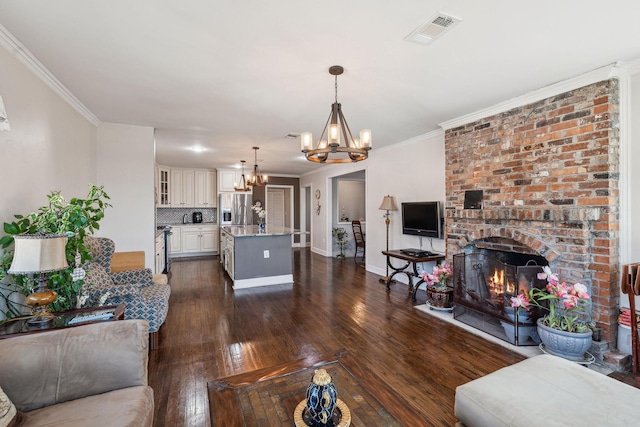 living room with dark wood finished floors, visible vents, ornamental molding, a brick fireplace, and a chandelier