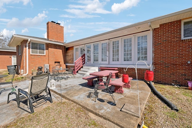 back of property with entry steps, brick siding, a patio, and a chimney