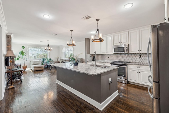 kitchen with stainless steel appliances, white cabinets, an island with sink, and light stone countertops