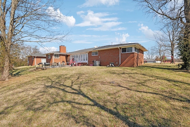 rear view of property with central AC unit, a patio, a chimney, a yard, and brick siding