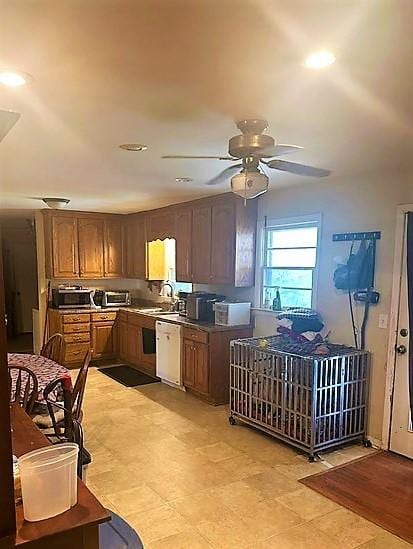 kitchen featuring dark countertops, brown cabinetry, a ceiling fan, a sink, and dishwasher