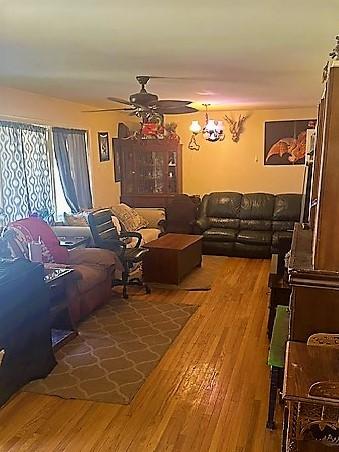 living area with ceiling fan with notable chandelier and wood finished floors