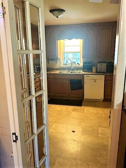 kitchen featuring white dishwasher, a sink, and light tile patterned floors