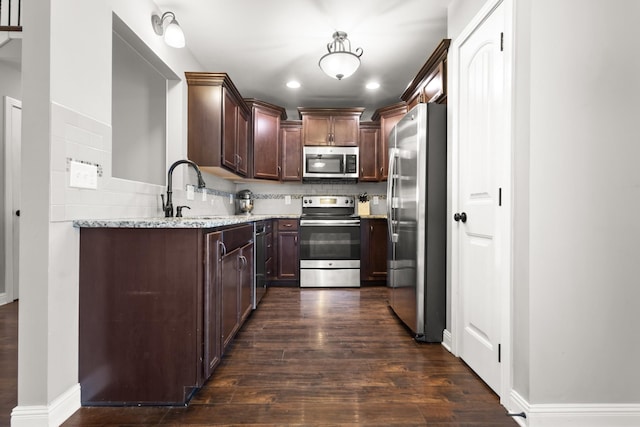 kitchen with light stone counters, dark wood-style floors, decorative backsplash, appliances with stainless steel finishes, and a sink