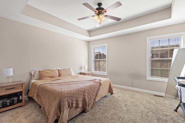 carpeted bedroom featuring a tray ceiling, visible vents, ceiling fan, and baseboards